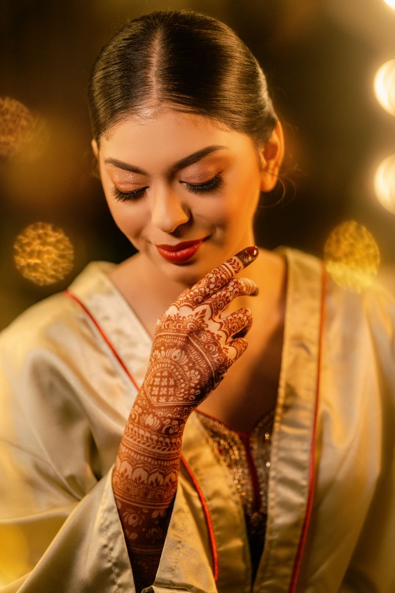Traditional Indian bridal look showcasing intricate henna design on hand and soft golden lighting in background.