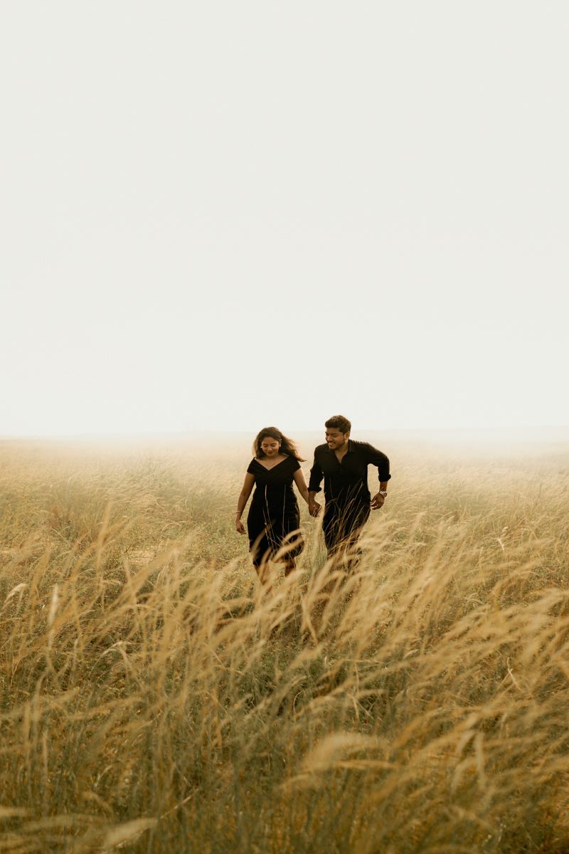 Couple running together through tall grass field in a dreamy landscape.