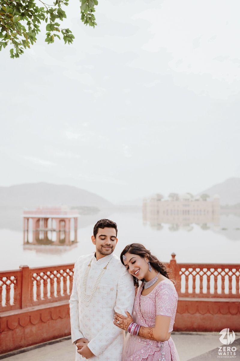 Romantic couple sharing a tender moment by a lakeside terrace with pink walls and mountains in the background.