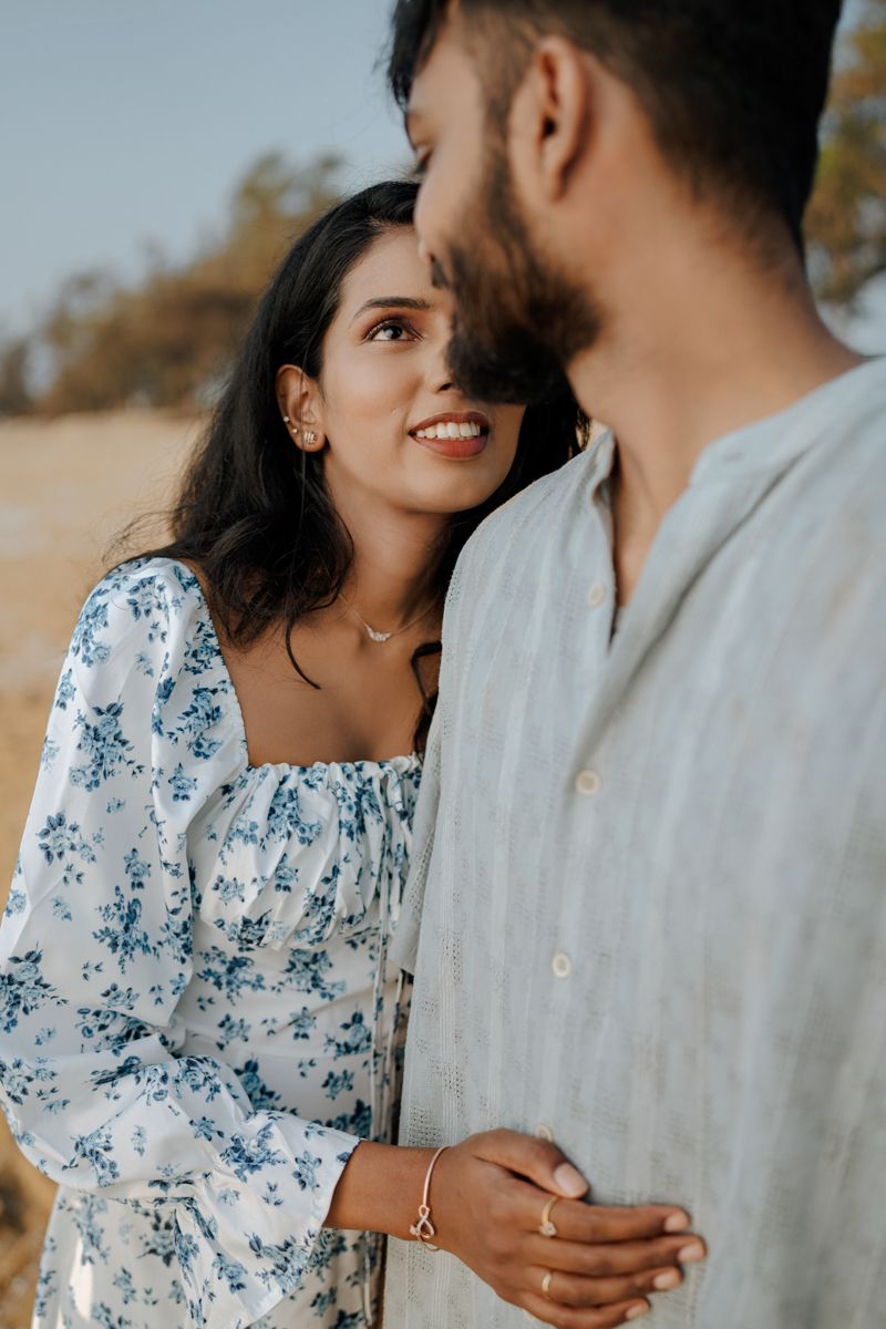 A couple shares an intimate moment on the beach while wearing coordinated blue and white outfits.