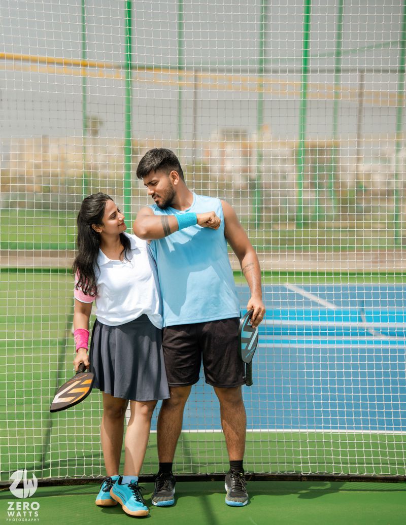 Playful interaction between two people on a tennis court with netting in the background.