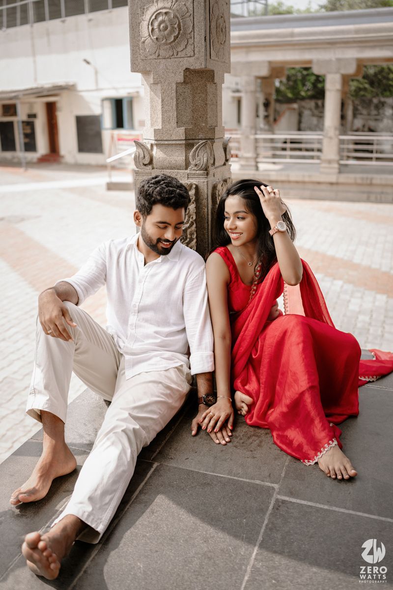 A couple in white and red outfits pose playfully on stone steps of a historic building.
