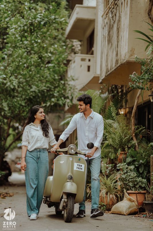 Vintage-themed couple photoshoot with scooter in tree-lined street.