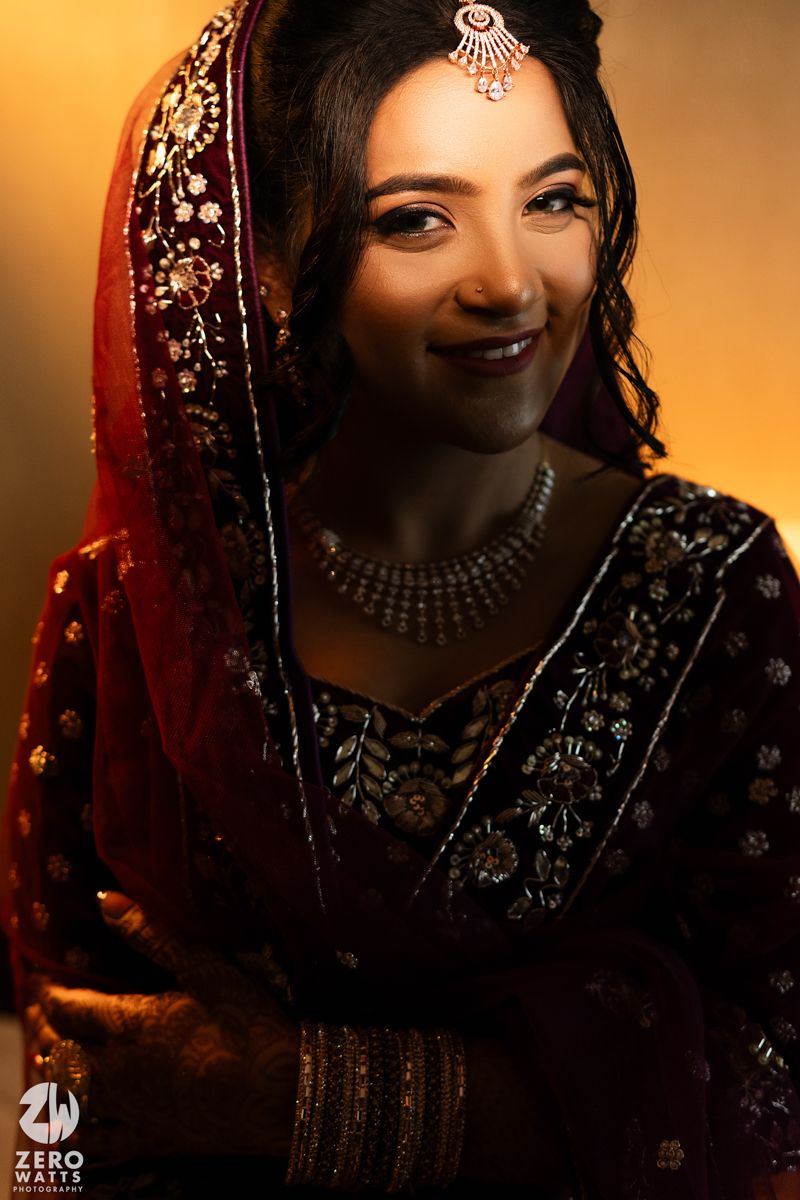 Close-up portrait of bride in dark burgundy attire with intricate jewelry and embroidered veil.