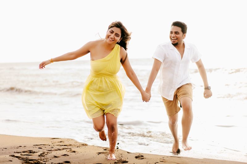Joyful couple running hand in hand on beach in white and yellow outfits.
