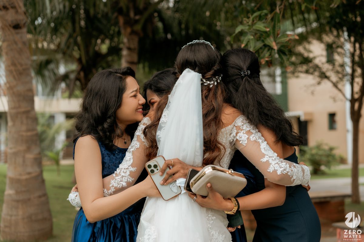 Bridesmaids in blue dresses share an emotional moment with the bride wearing a white gown and veil.