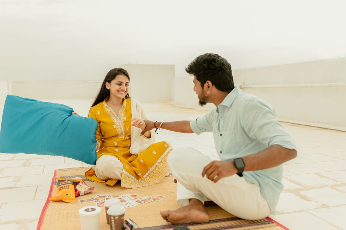 Two people sharing a meal while sitting on the floor with food and drinks laid out on a white surface.