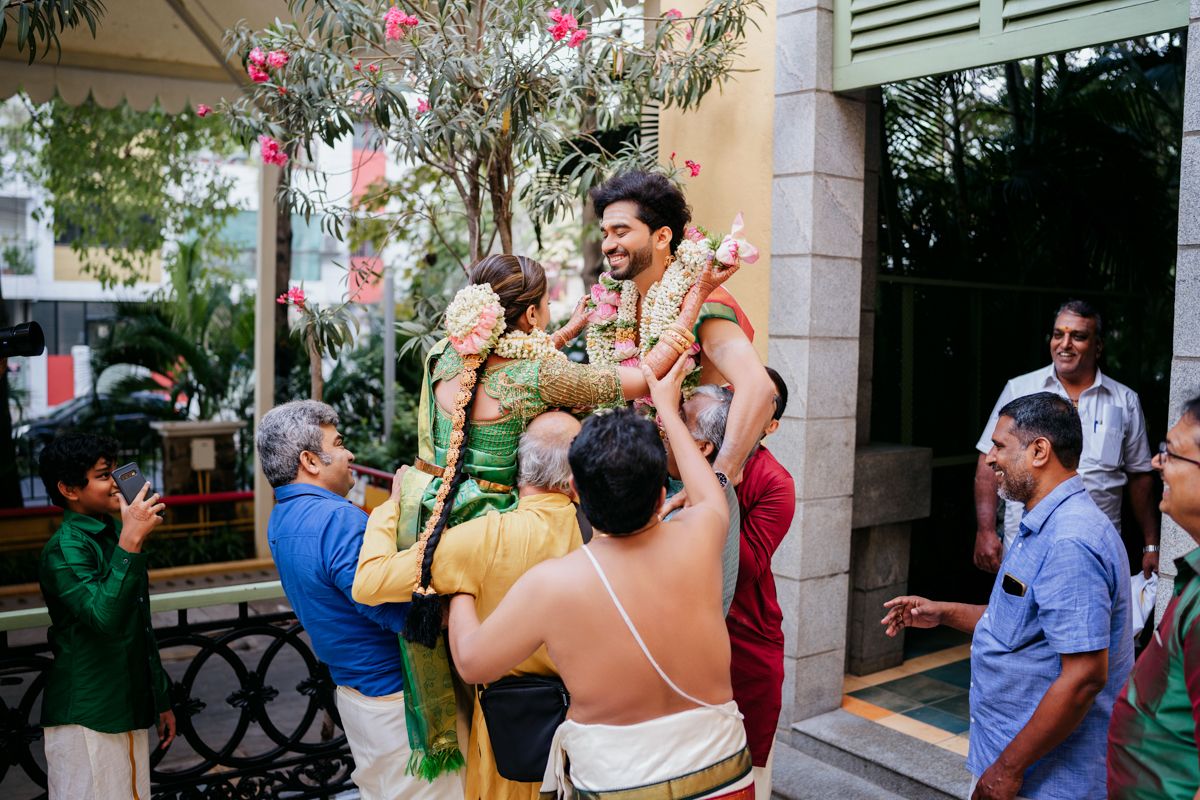 Wedding guests celebrate and lift people during festivities outside a decorated venue.