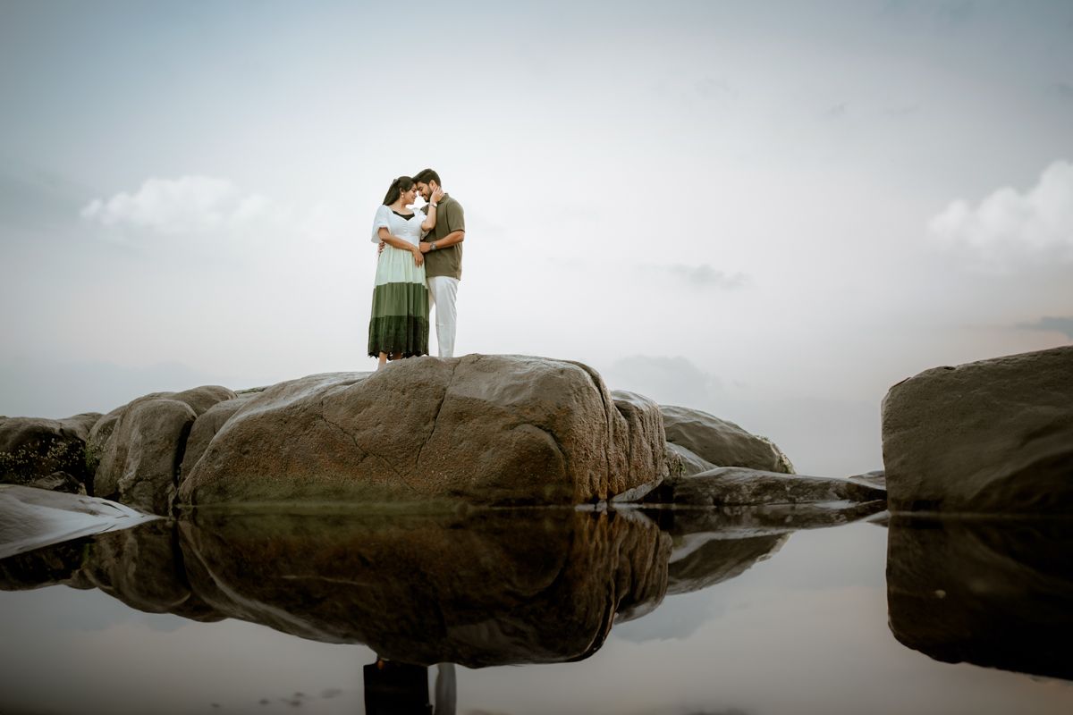 Silhouetted couple standing on rocky outcrop reflected in still water.