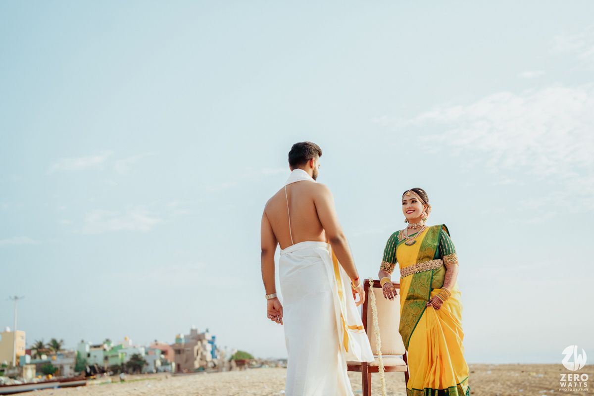 Traditional South Indian couple in wedding attire standing on beach.