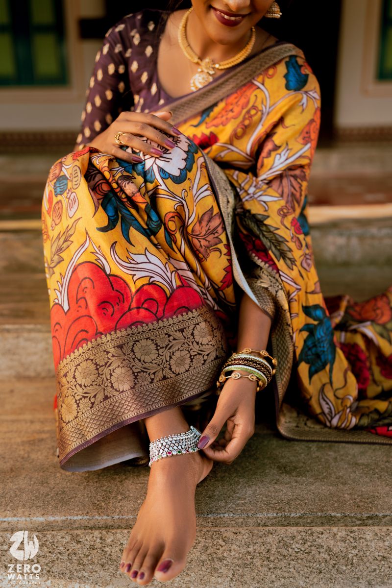 Close-up of ornate yellow and red silk saree with intricate patterns and traditional Indian jewelry details.