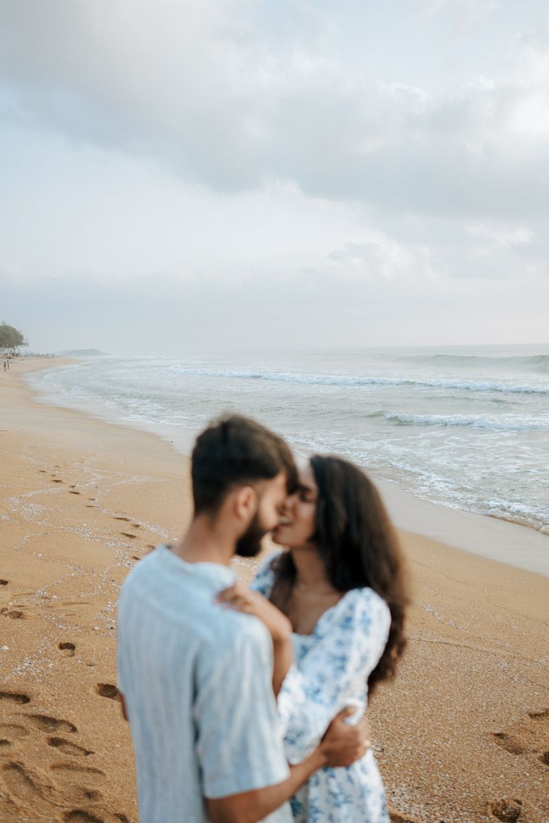A couple sharing an intimate moment on a sandy beach with gentle waves rolling in.
