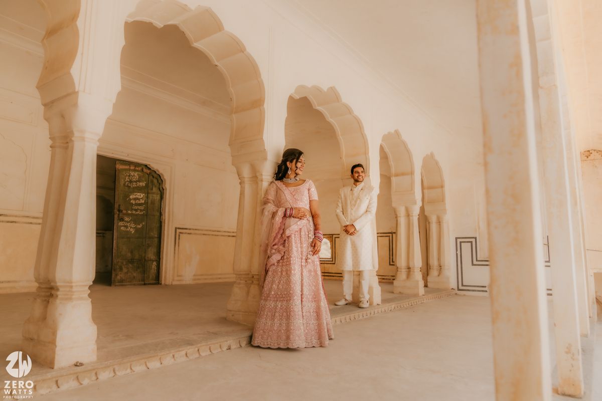 A couple walks together in an ornate corridor with white arched pillars in traditional Indian palace architecture.
