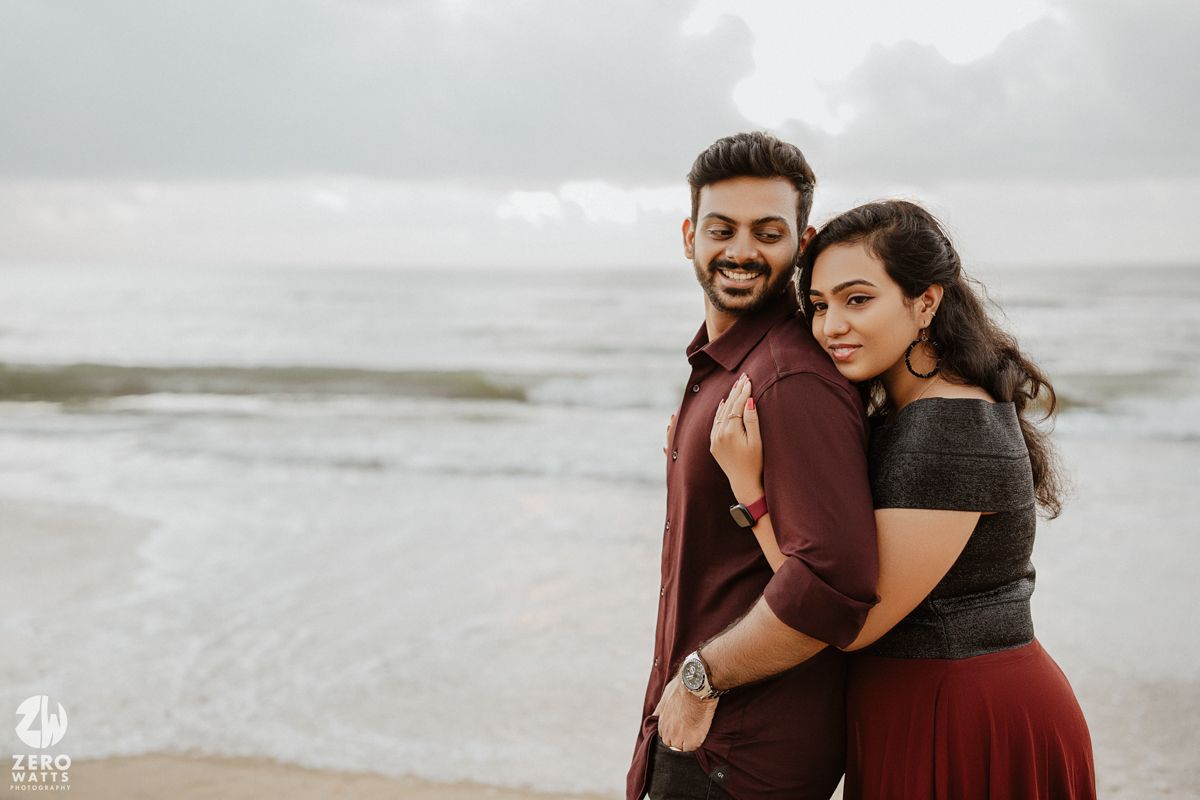 A happy couple shares an intimate moment at a beach during overcast weather.