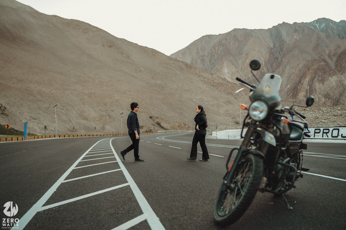 A vintage motorcycle parked on a desolate mountain highway with rugged peaks in the background.
