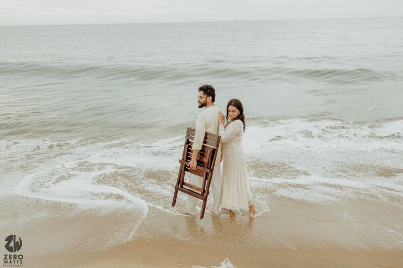 Couple in casual attire walking along a serene beach with gentle waves.