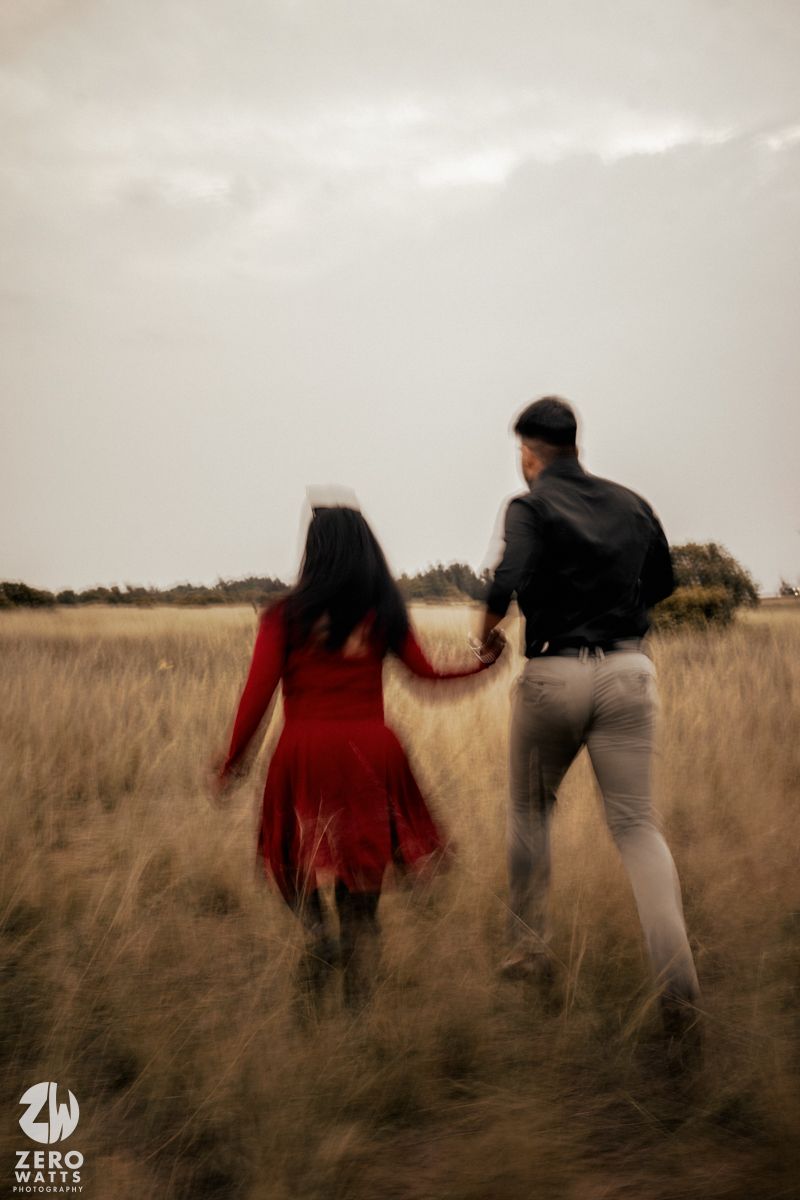 Couple walking through tall grass field during golden hour.