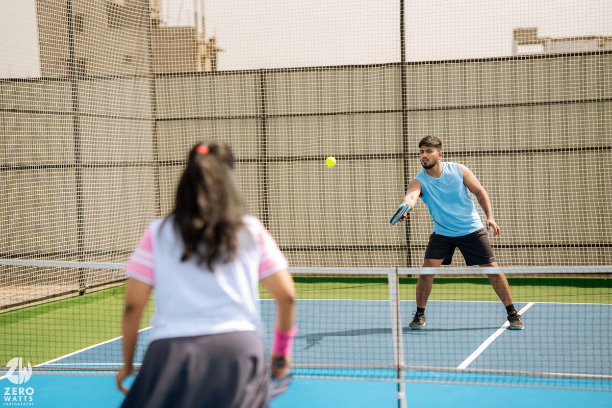 Two players competing in a friendly game of pickleball on a bright blue court.