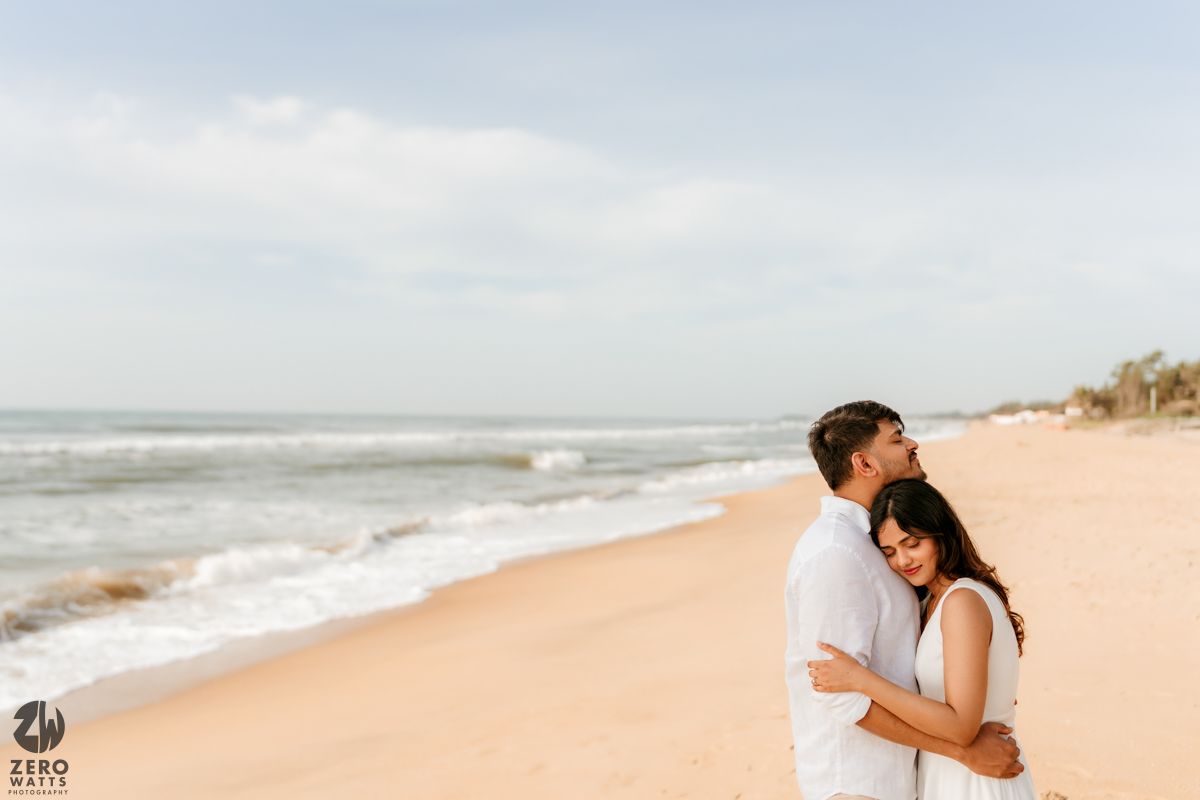 Wide angle beach landscape showing couple embracing on empty shoreline.