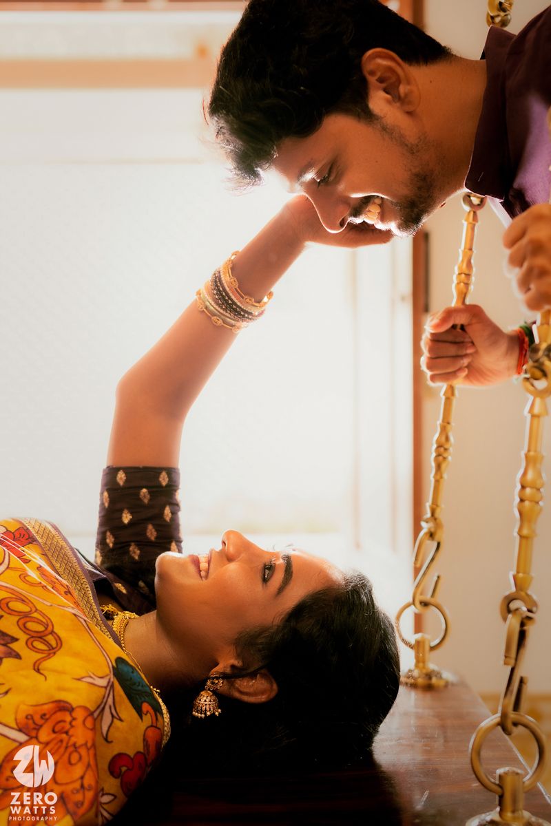 Romantic couple in traditional Indian attire pose intimately near decorative golden swing.
