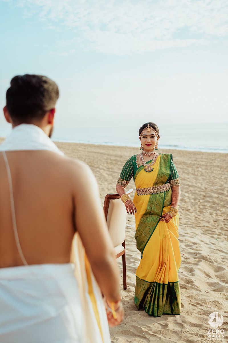 Couple in traditional South Indian wedding attire posing for photos on a sandy beach during golden hour.