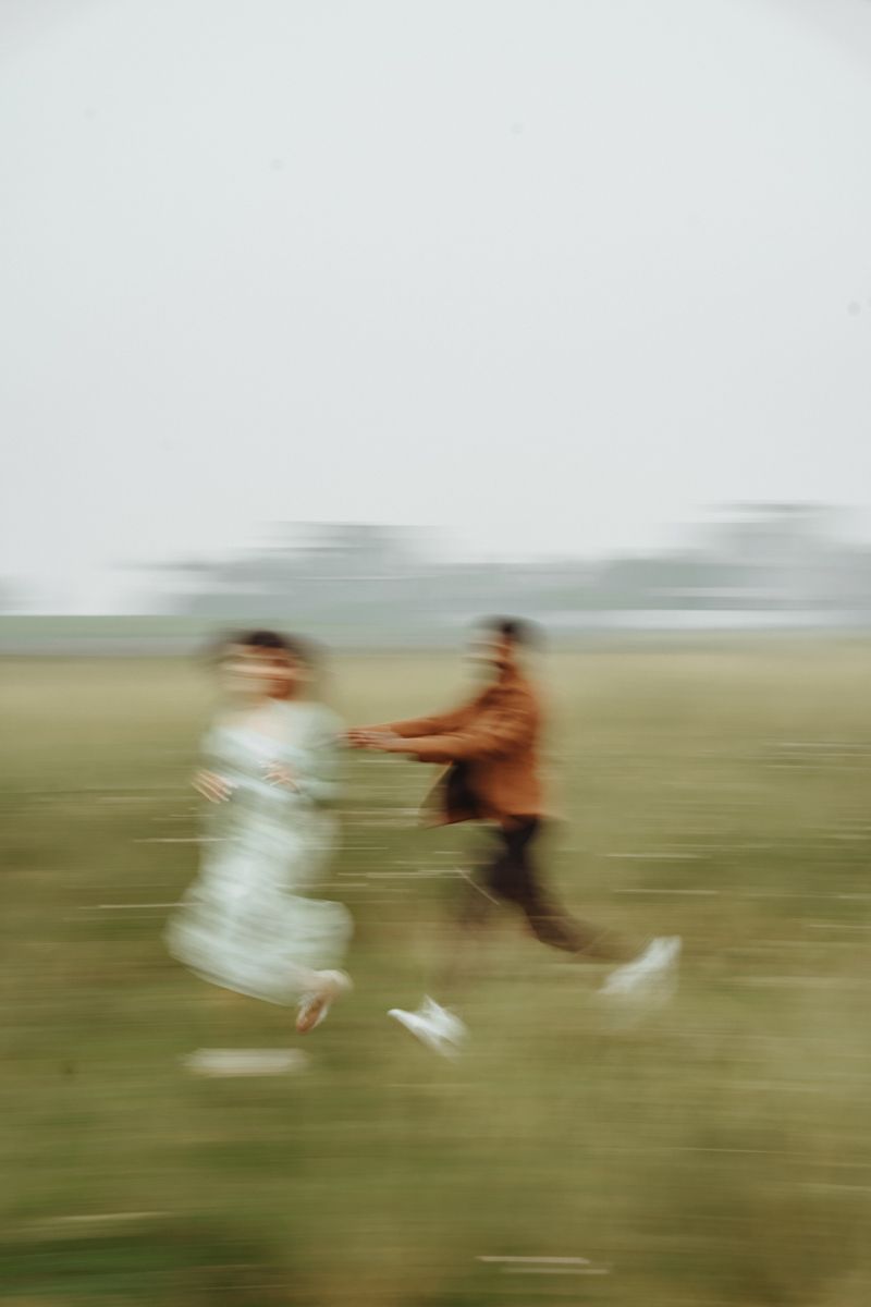 Motion blurred photograph of two people running and playing in a misty green field with ethereal lighting.