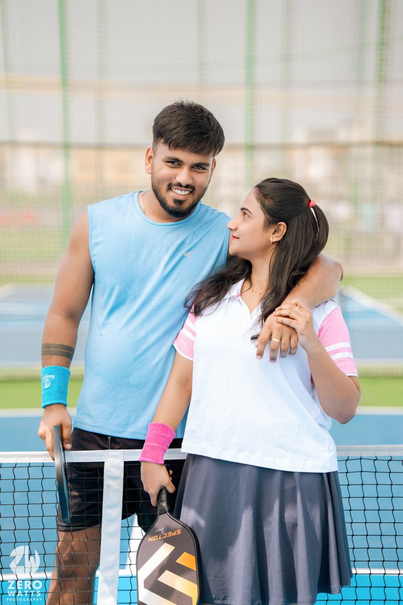 Two people standing close together on a tennis court having a playful moment.