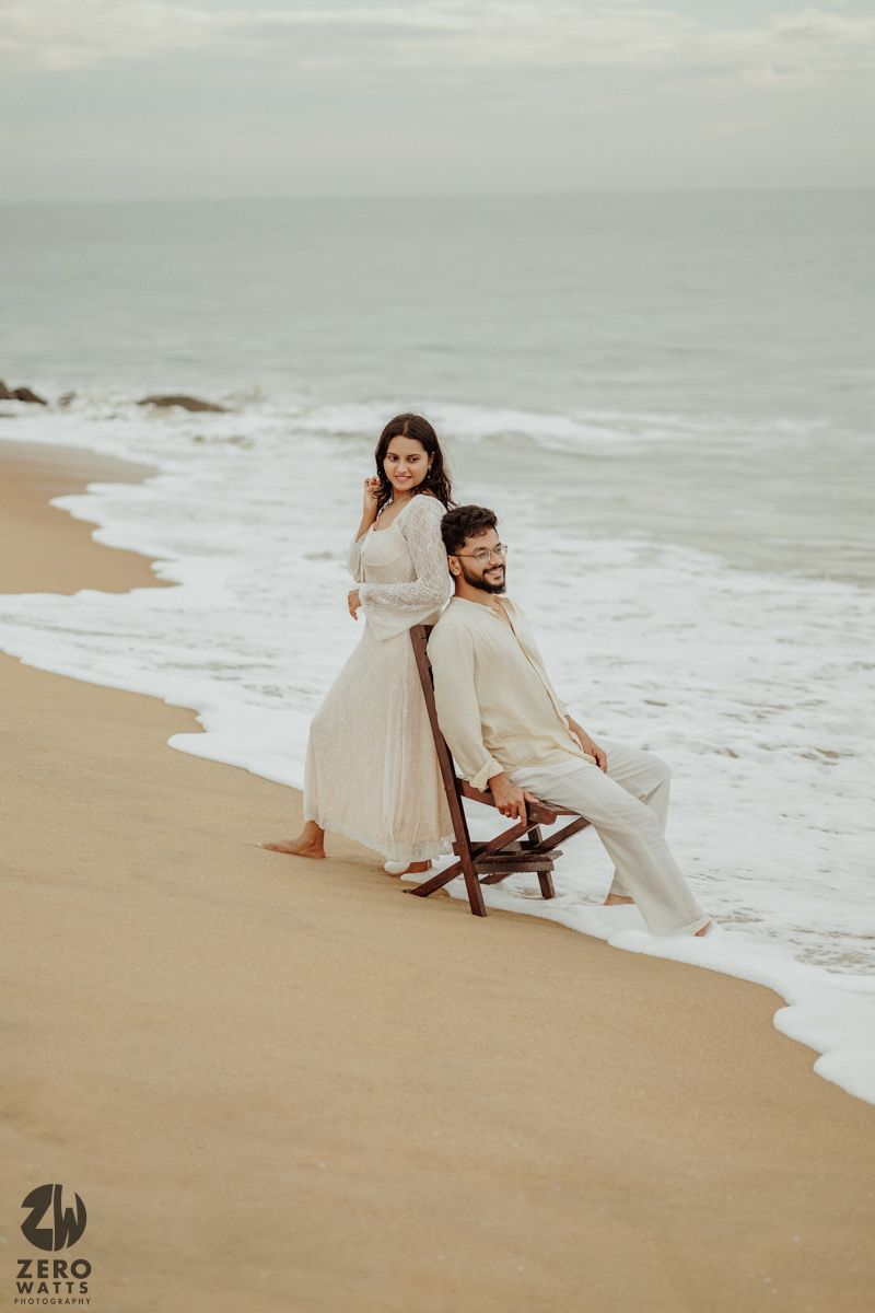 A romantic beachside photoshoot with waves crashing on a sandy shore in overcast weather.