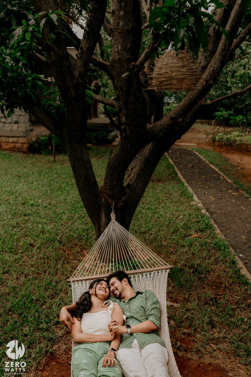 Romantic couple relaxes together in a white hammock under shady trees in a peaceful garden setting.