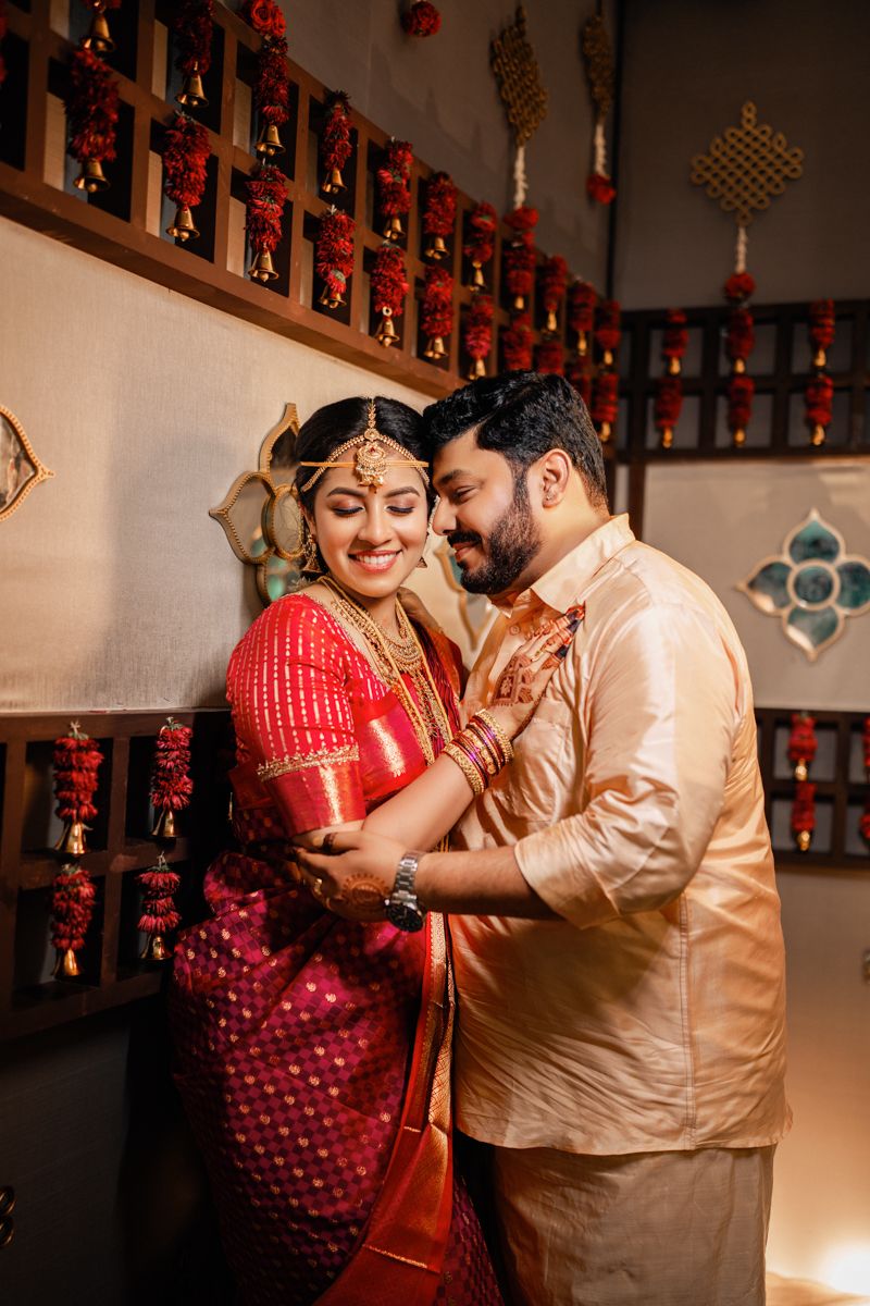 Traditional South Indian couple in wedding attire embrace in decorated indoor setting with red lanterns.