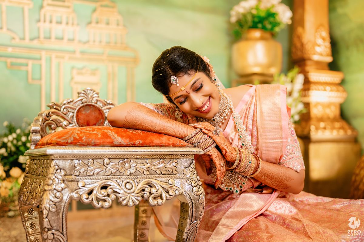 A person in a pink and gold traditional South Asian saree rests gracefully on an ornate silver table in an elegant setting.