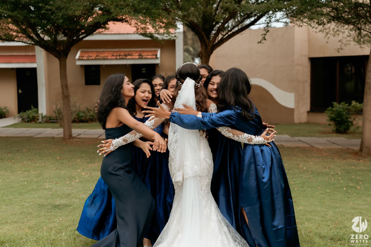 Wedding party wearing navy blue dresses hugging and celebrating together outdoors.