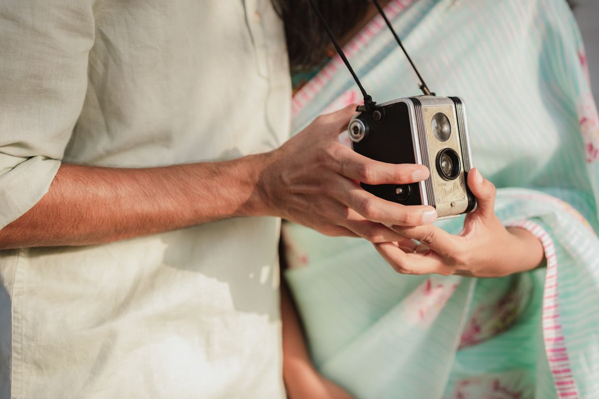 Hands hold a vintage twin-lens reflex camera against a pastel background of white and mint green clothing.