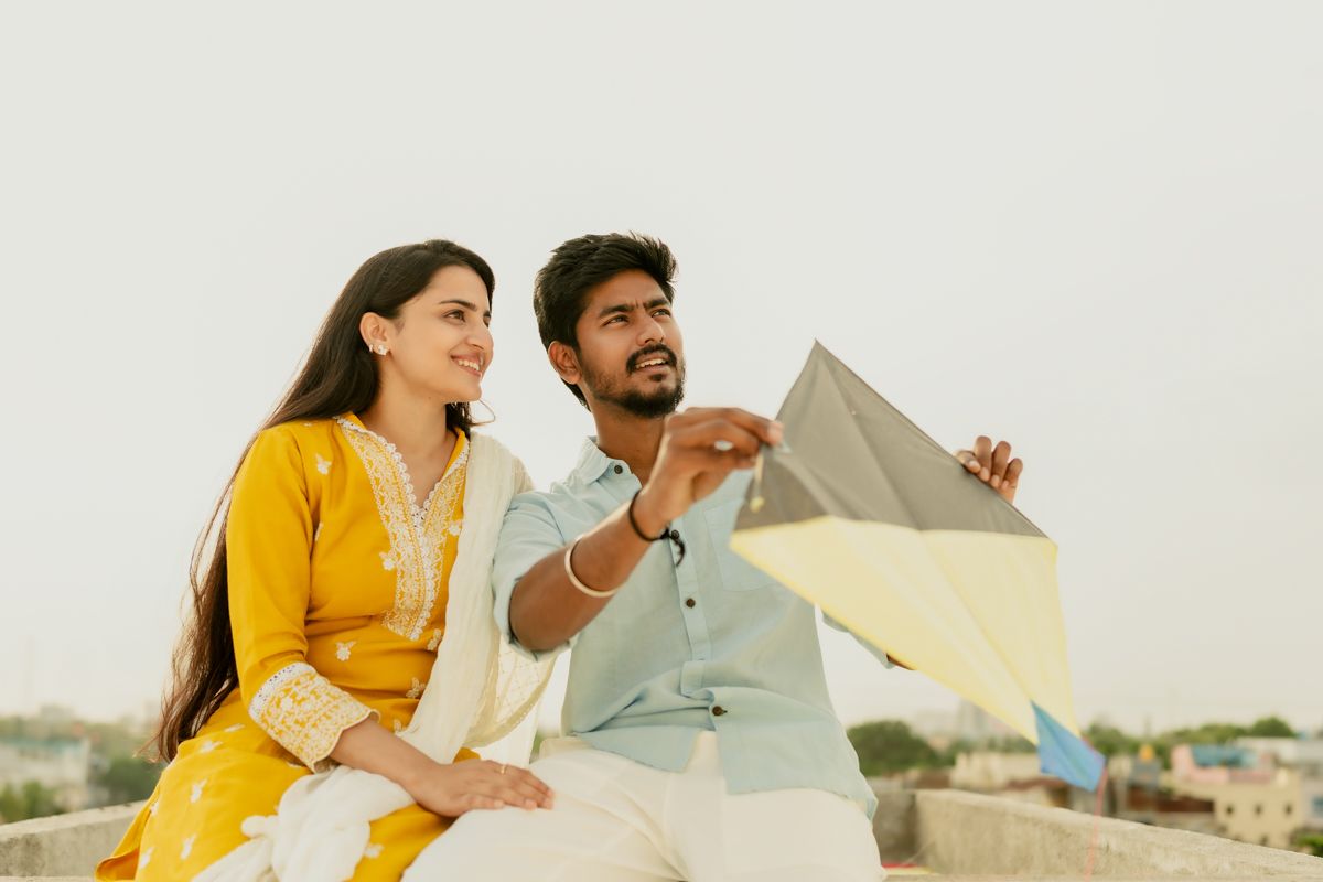 A couple in traditional Indian attire flying a kite together on a rooftop during a bright sunny day.