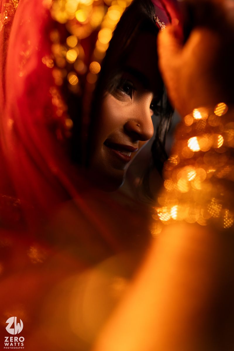 Artistic portrait with warm lighting showing a red dupatta and bokeh lights in the background.