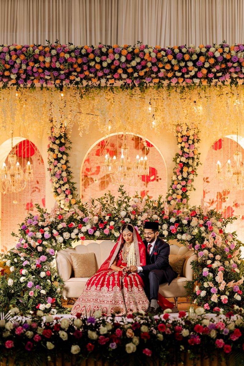 Elegant Indian wedding stage decorated with pink and white roses featuring a beige couch against an arch backdrop.