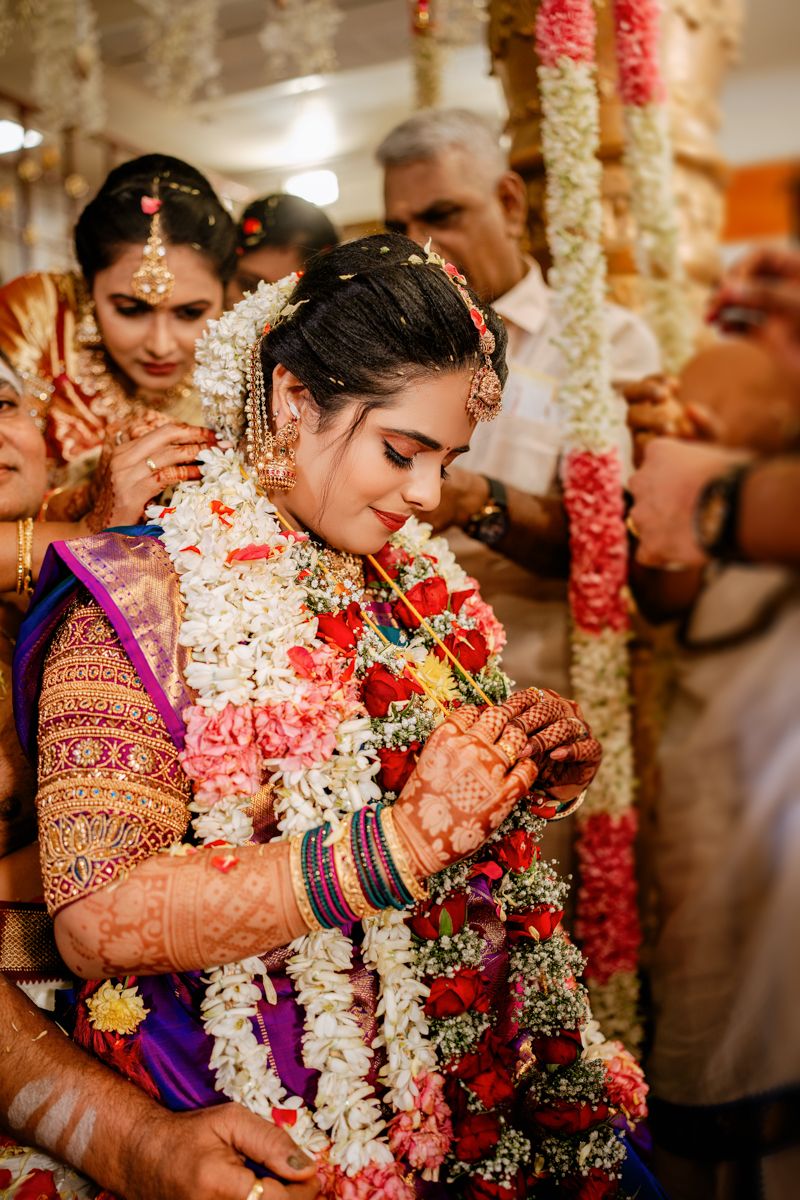 Traditional Indian wedding ceremony with colorful floral garlands, ornate sari, and henna-adorned hands during an intimate moment.