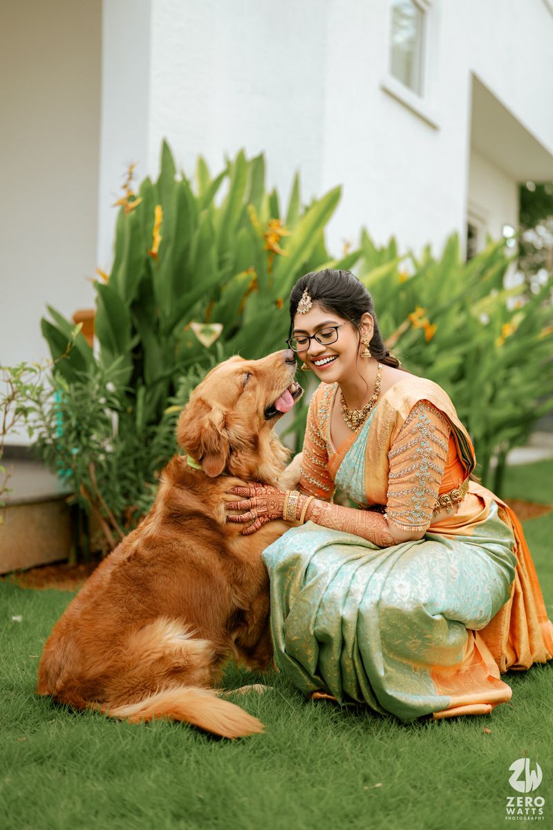 A heartwarming moment shared between a golden retriever and someone in traditional Indian attire sitting on grass near flowering plants.
