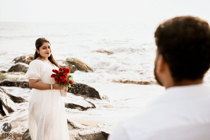 A romantic seaside photoshoot featuring white attire and red roses against a bright background.