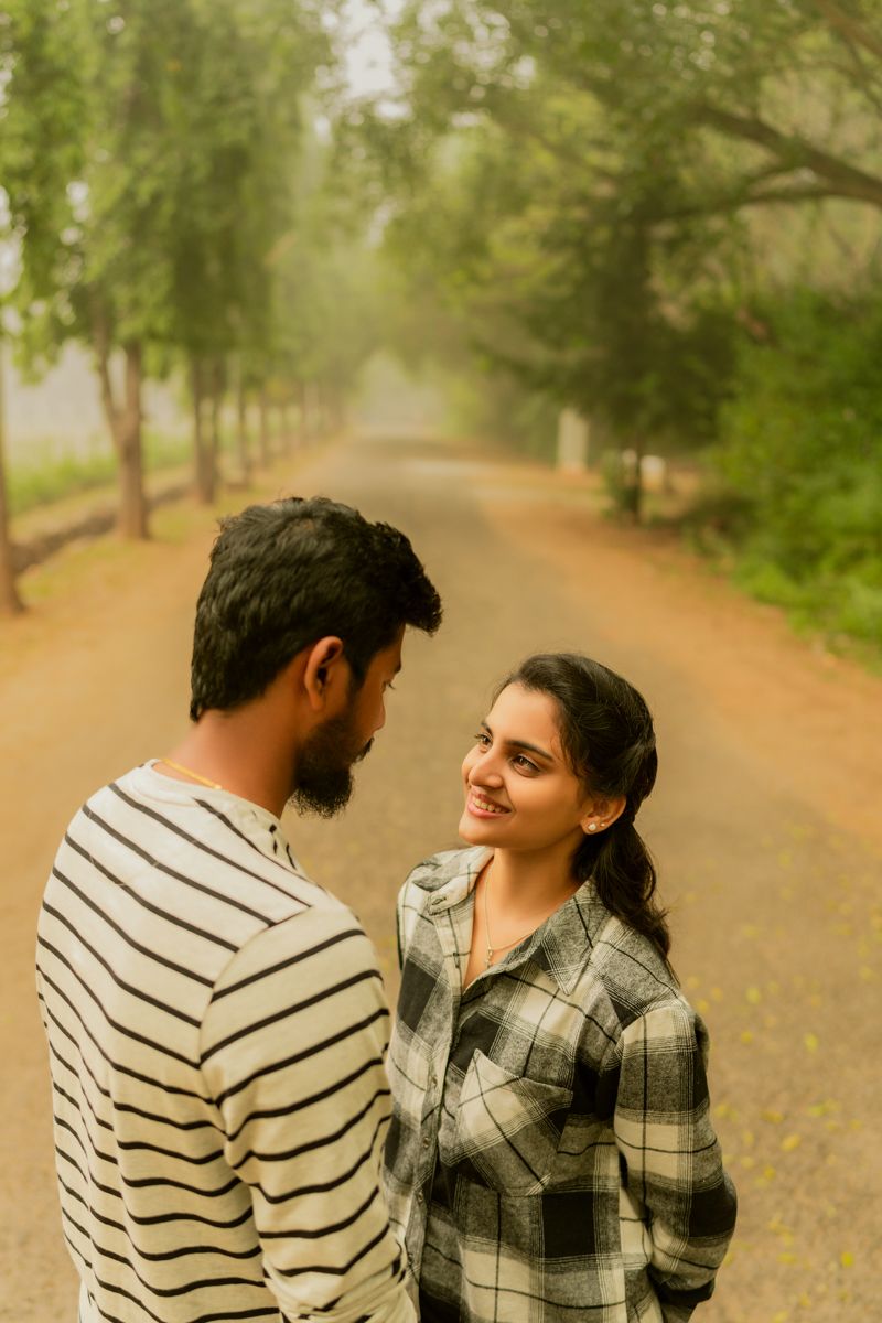 A couple shares a romantic moment on a tree-lined path in a misty park setting.