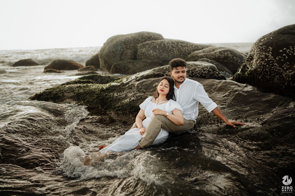Romantic couple relaxing on coastal rocks during sunset photoshoot.
