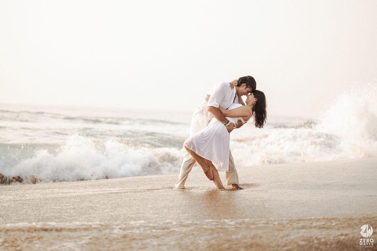 Couple dancing together on beach with crashing waves and soft sunlight.