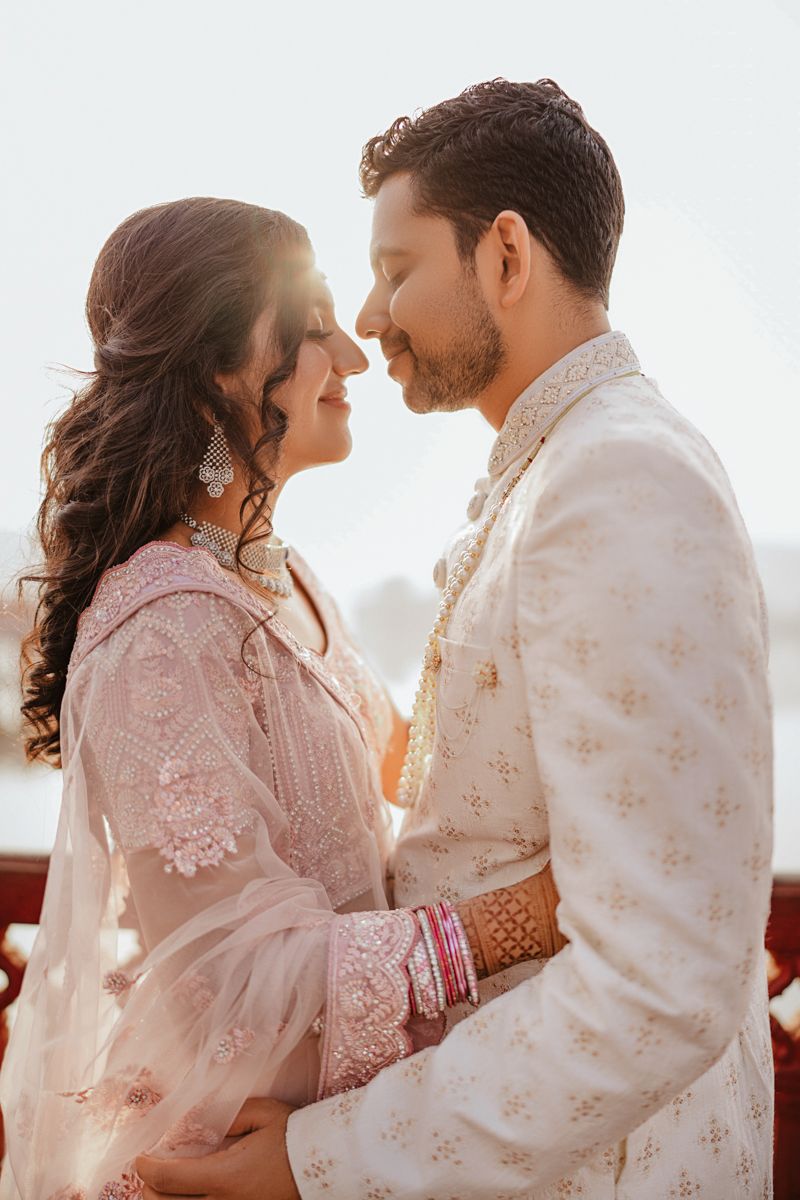 A couple in elegant traditional Indian wedding attire share an intimate moment during golden hour.