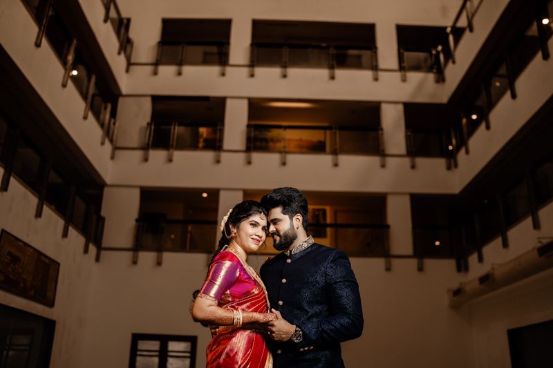 Couple in formal attire share intimate moment in luxurious hotel atrium with dramatic lighting and architectural details.
