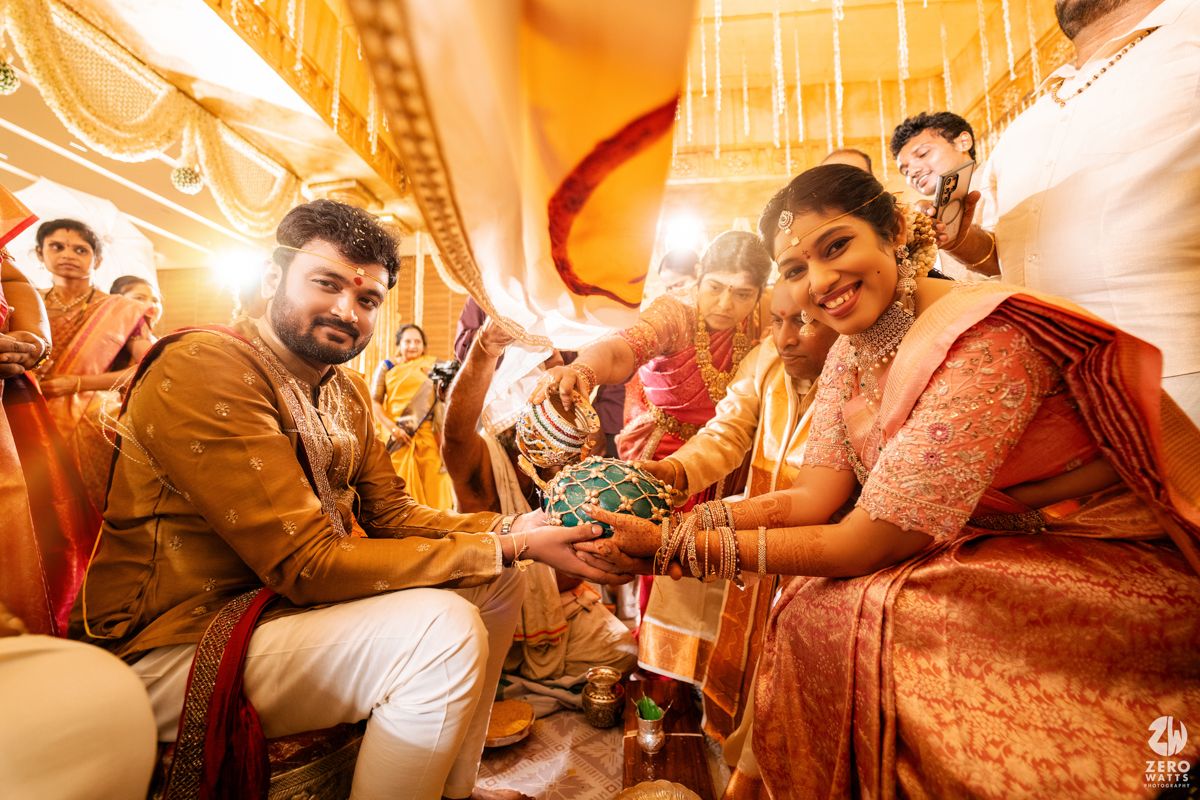 Traditional Indian wedding ceremony moment captured with warm lighting and guests in ethnic attire in an ornate setting.