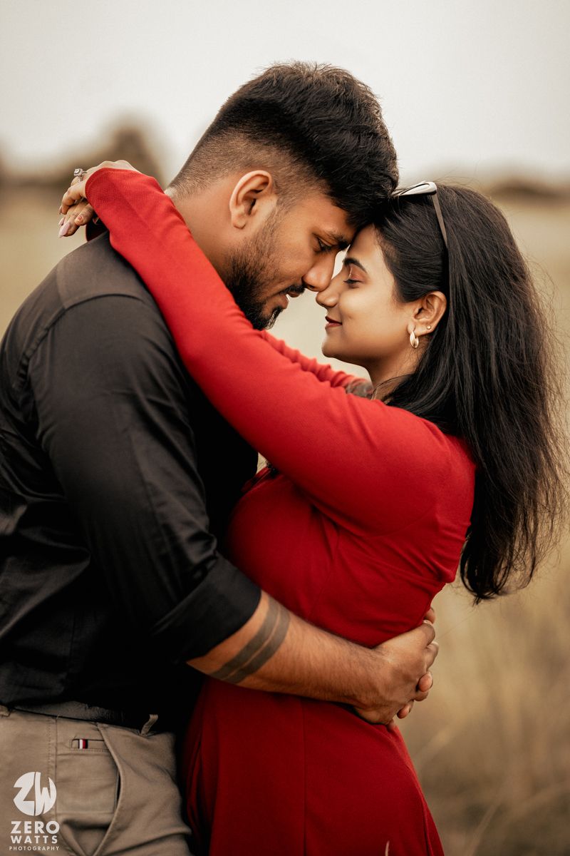 An intimate moment between a couple embracing in a field wearing red and black outfits.
