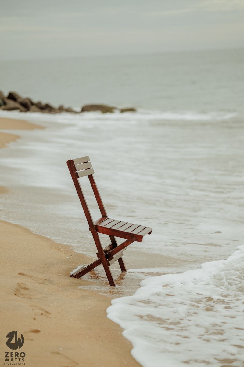 Wooden chair standing alone on beach as waves wash up on shore.