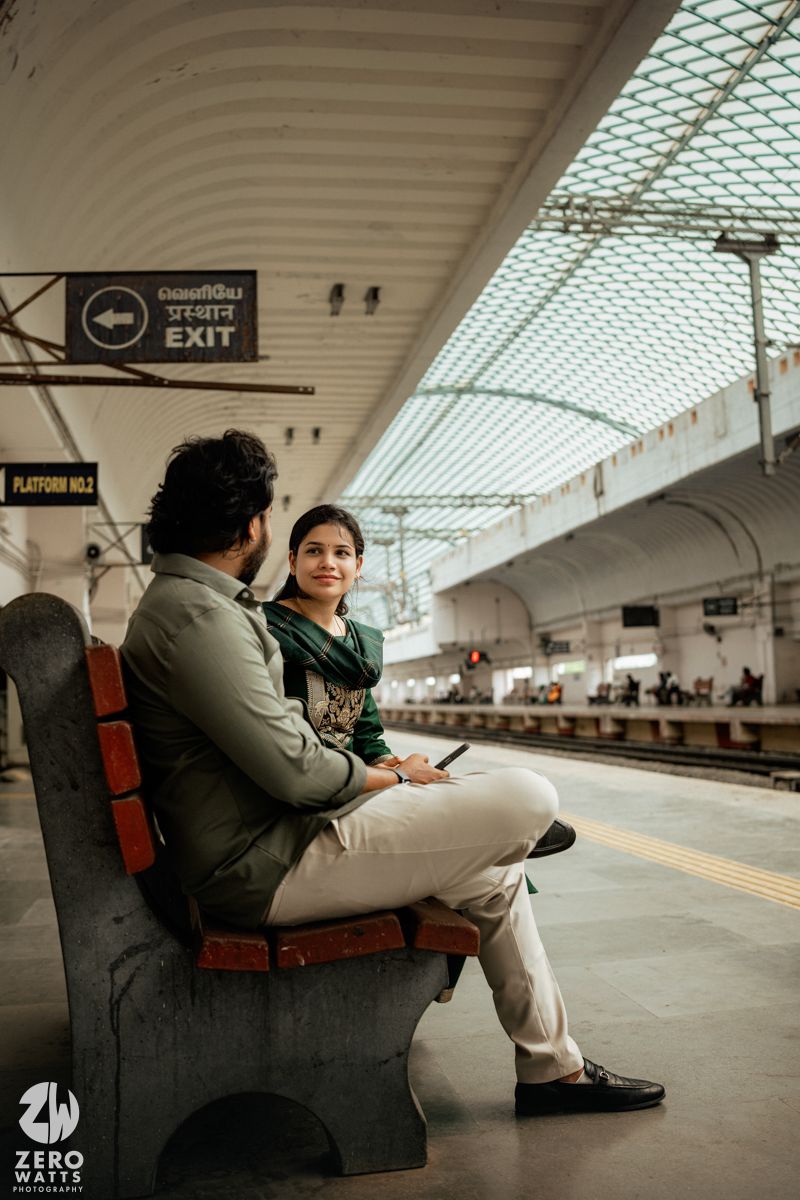 Modern railway platform with arched ceiling and exit signs provides backdrop for seated couple.