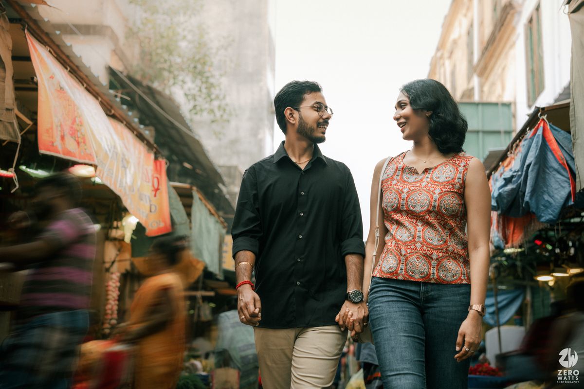 Stylish couple walking and laughing together through a bustling market street.