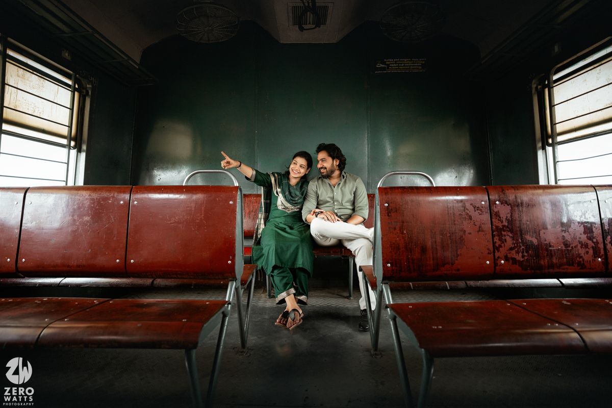 A couple sitting together on red seats in a vintage train car enjoying a playful moment.